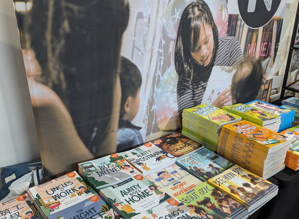 Natventure pop-up booth: a table of Singapore children's books in front of a backdrop of Cecilia reading to children